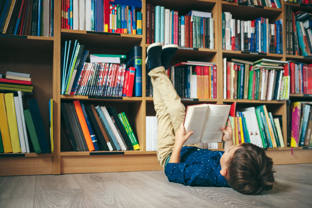 Bub liegt in Bibliothek am Boden und liest.
